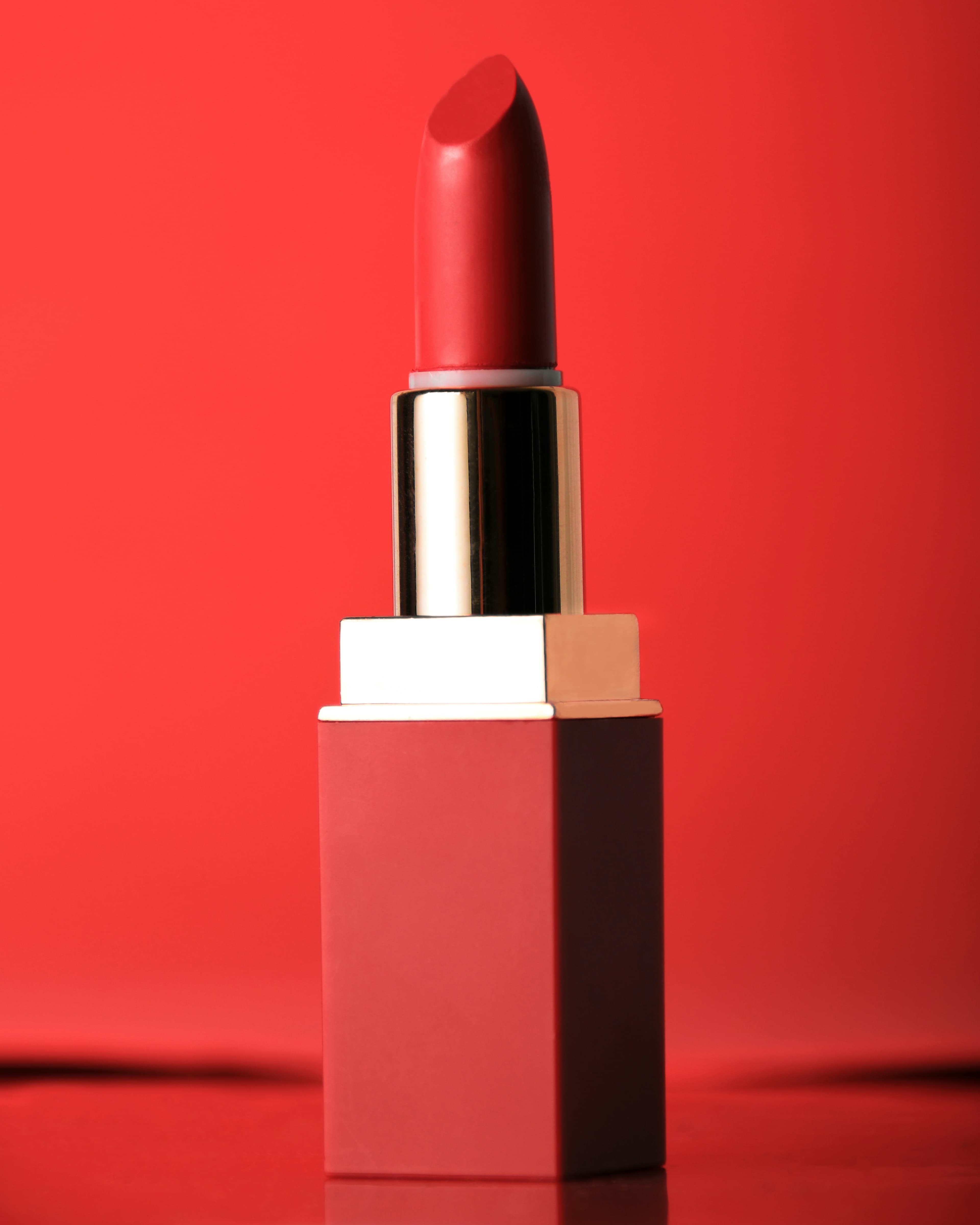 Velvet Lip Color in Nude. Red lipstick standing on a red surface