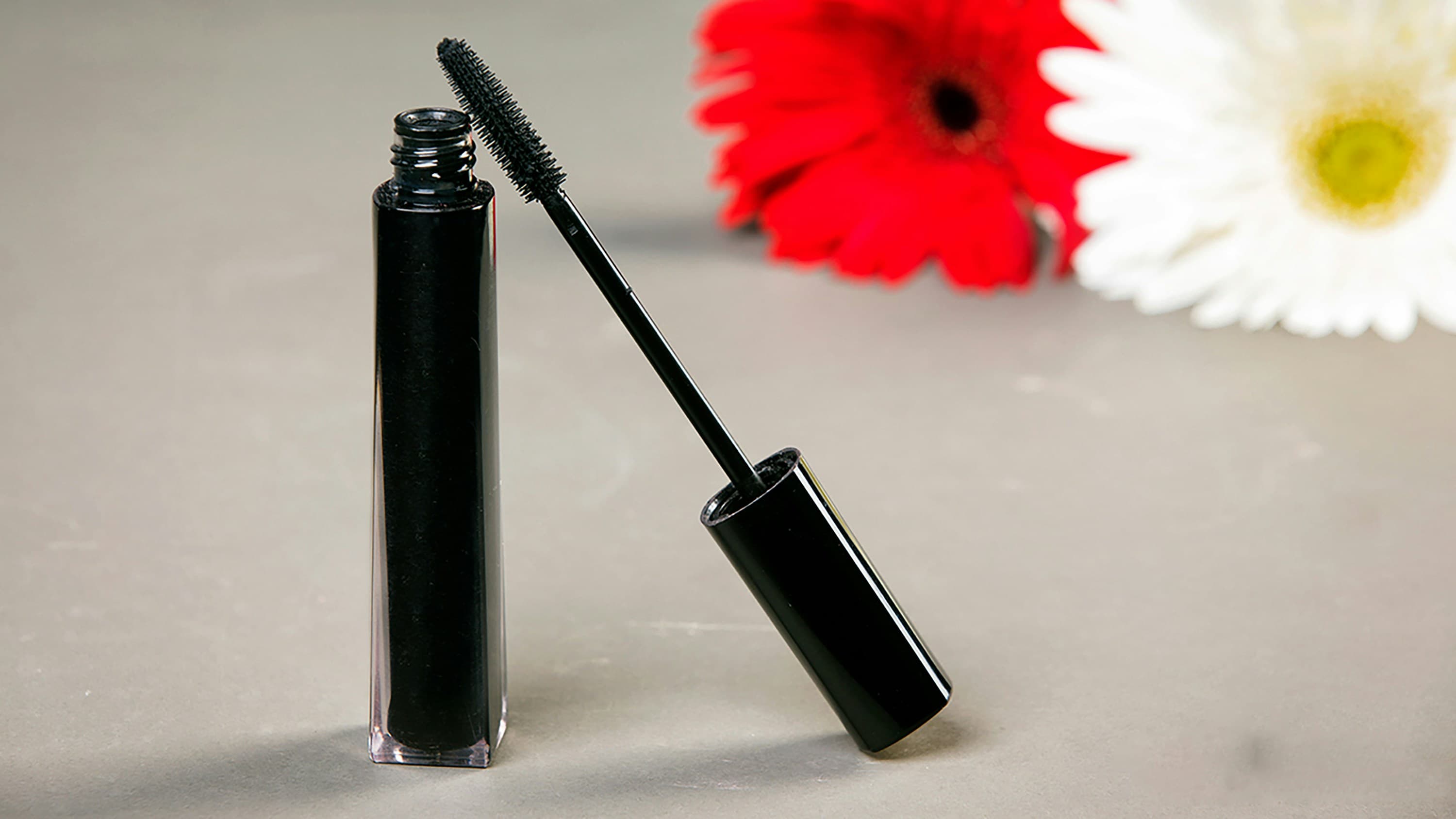 Sculpt Mascara in Noir. Black mascara tube and wand beside a red flower